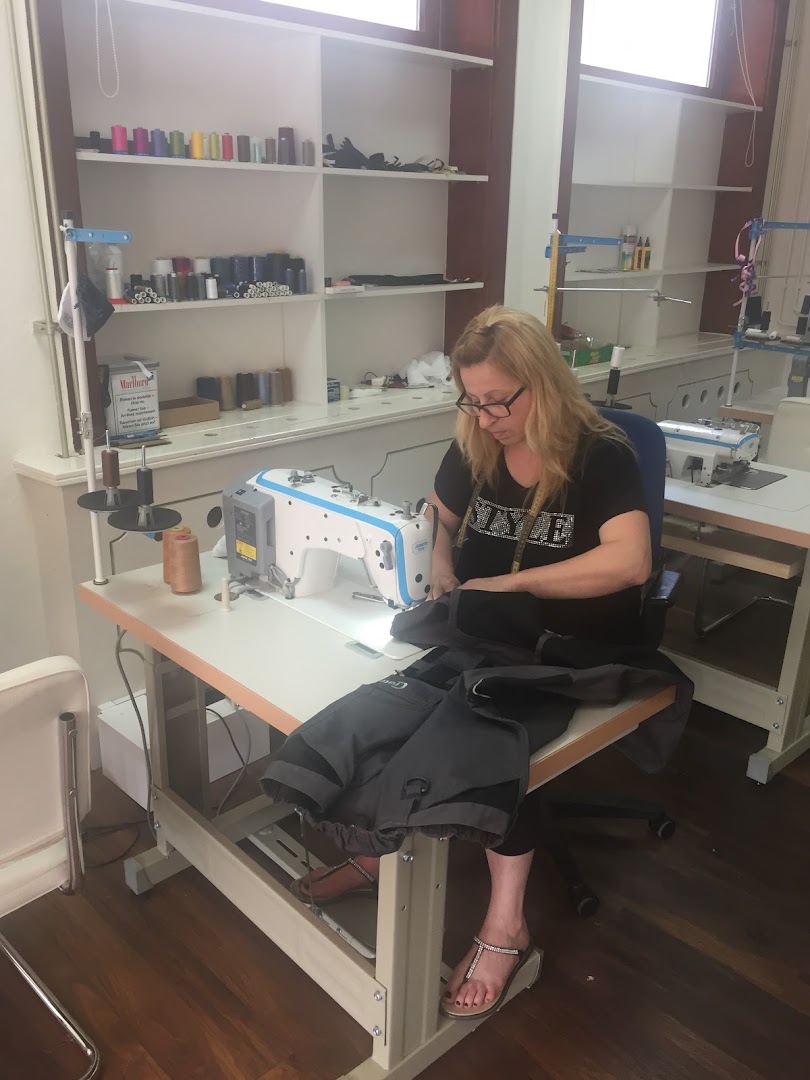 Miki achter de industriële naaimachine in het atelier aan de Molenstraat, met een rek vol garenkleuren op de achtergrond